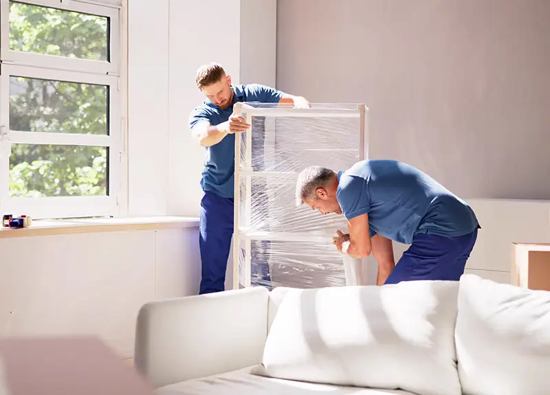 Zwei Umzugshelfer verpacken ein Regal für den Umzug