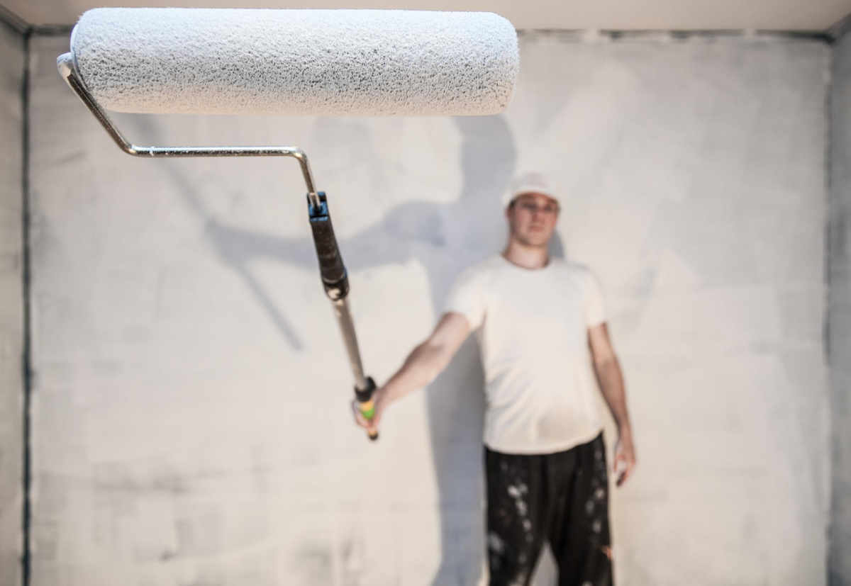 Mann hält Malerrolle vor weißer Wand.