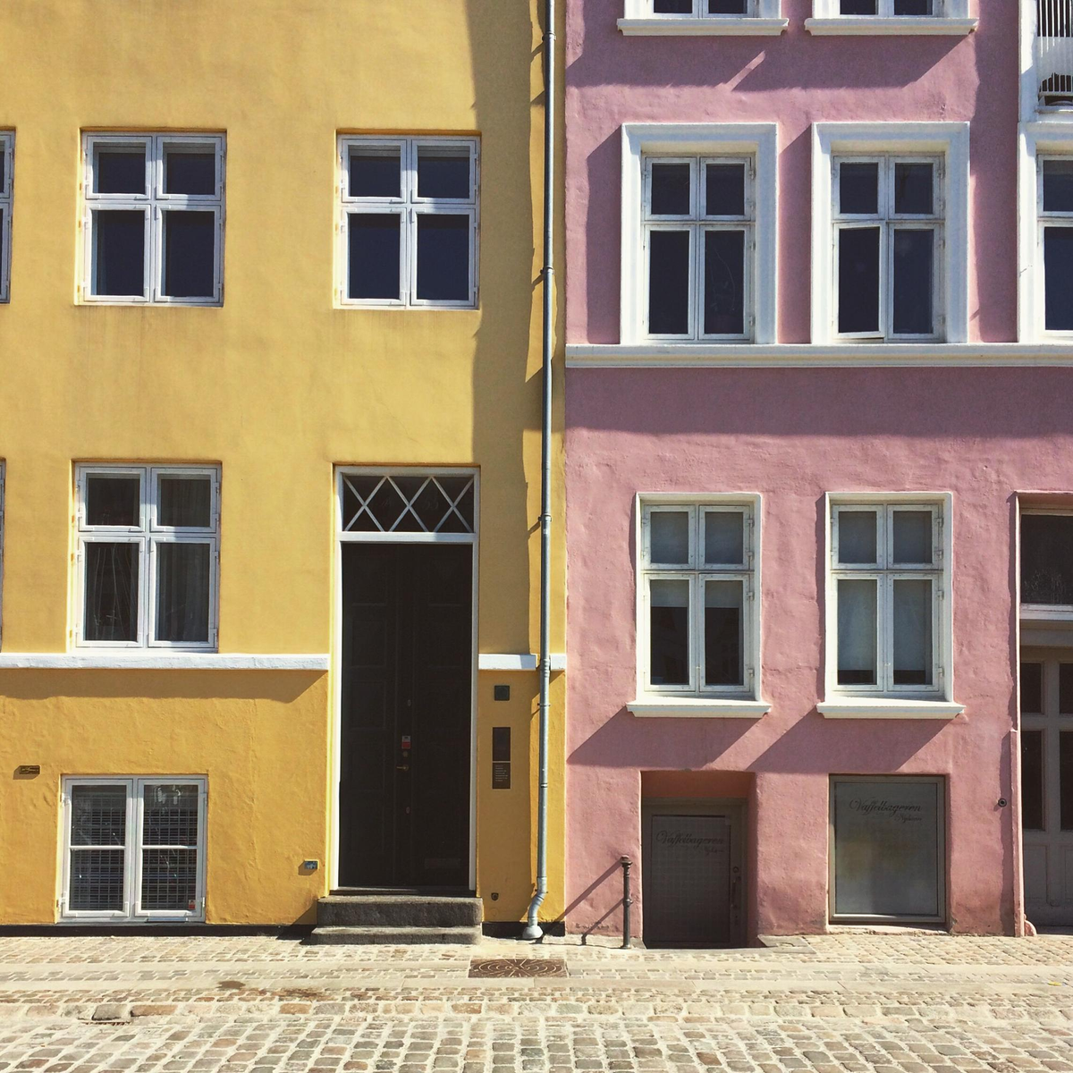 Zwei bunte Stadthäuser in Gelb und Rosa nebeneinander.