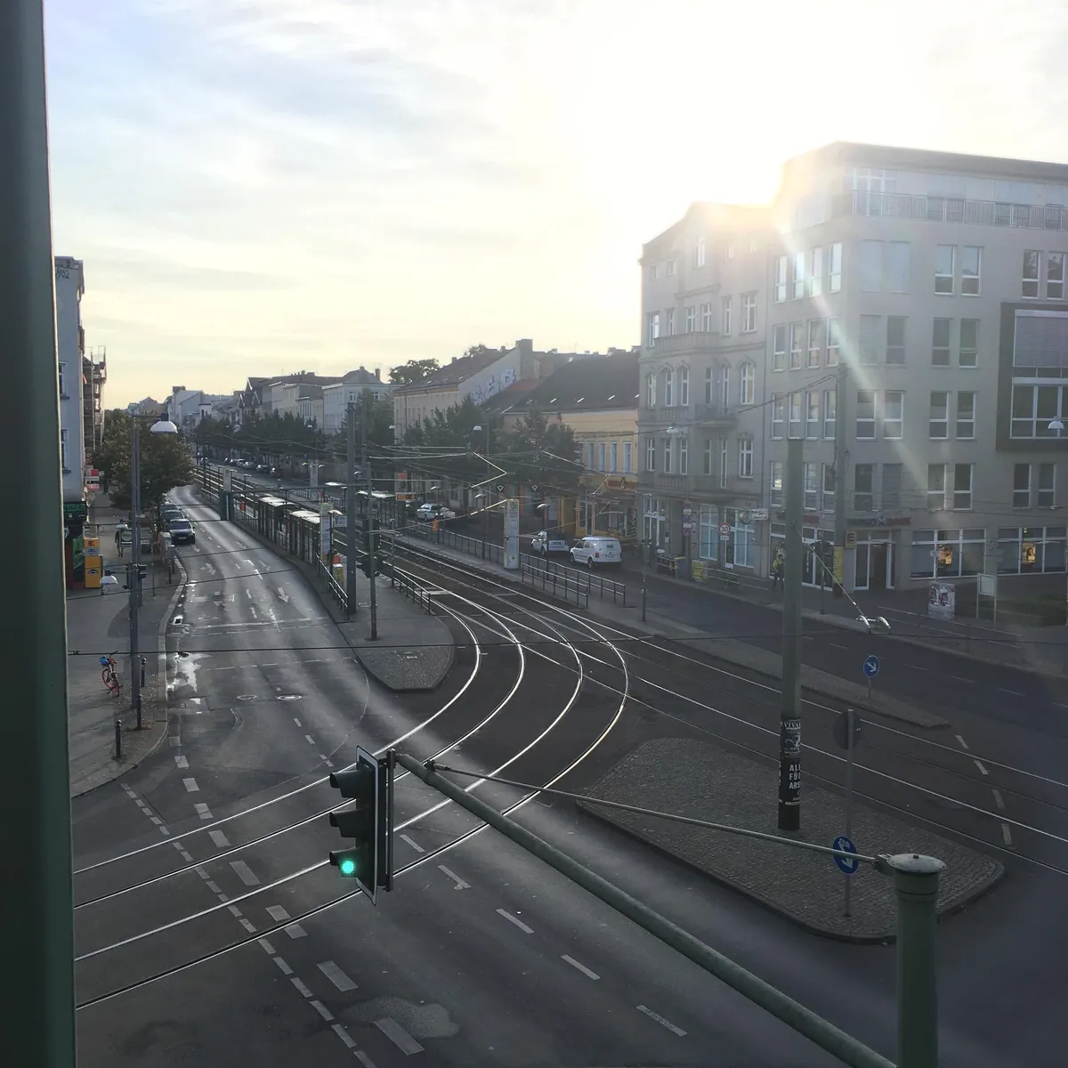 Leere Stadtstraße mit Straßenbahnschienen bei Sonnenaufgang.