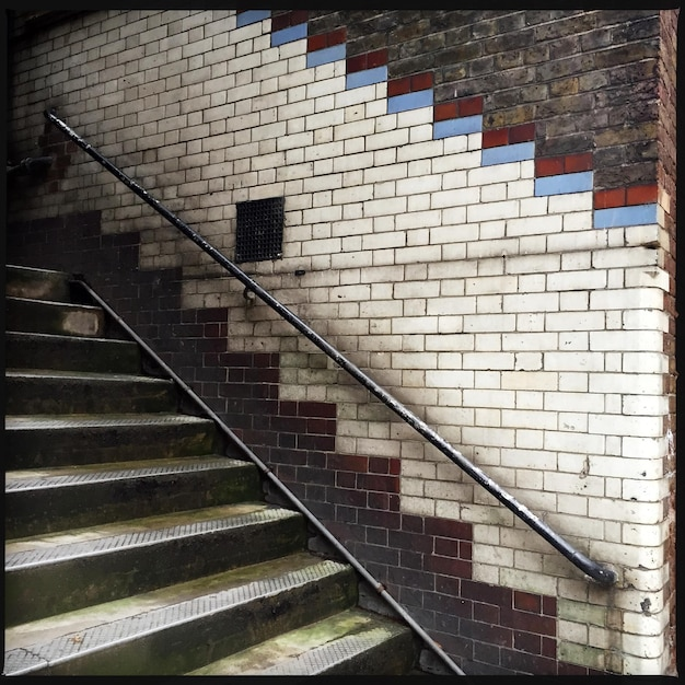 Alte Steintreppe mit Metallgeländer an gefliester Backsteinwand.