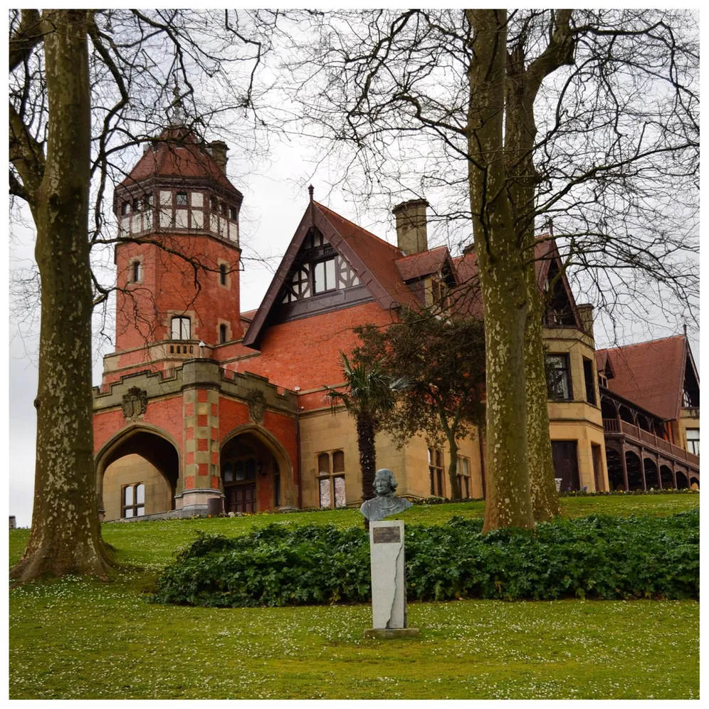 Historische Villa mit Turm, Büste und kahlen Bäumen.