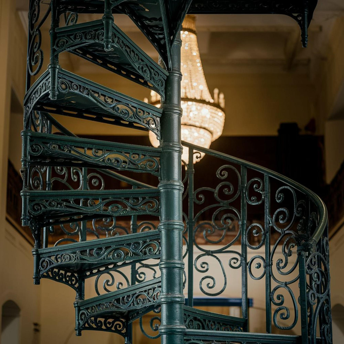 Elegante gusseiserne Wendeltreppe mit Kronleuchter im Hintergrund.